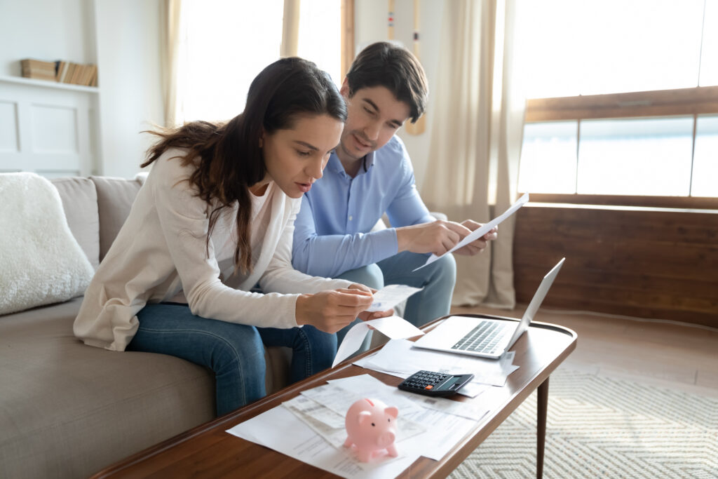 Concentrated millennial couple sitting on couch involved in reading documents to get their mortgage preapproved